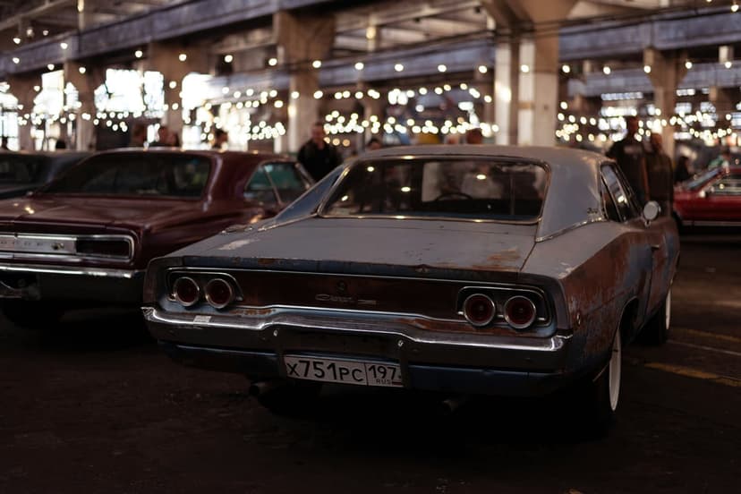 Rusty Dodge Charger and vintage muscle cars parked in a dimly lit hall decorated with glowing string lights.