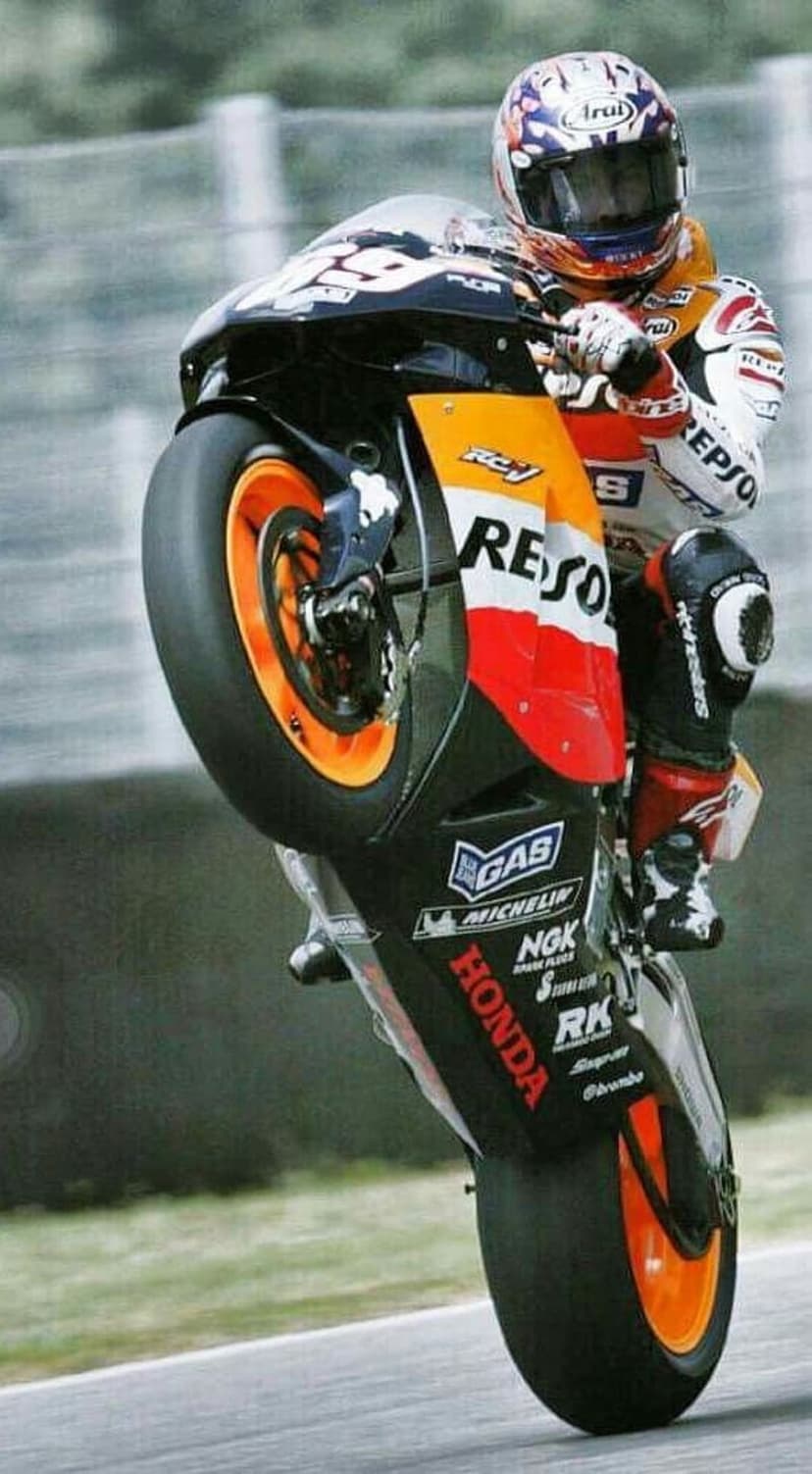 Professional motorcycle racer in an orange suit performs a wheelie on a blurred asphalt race track.