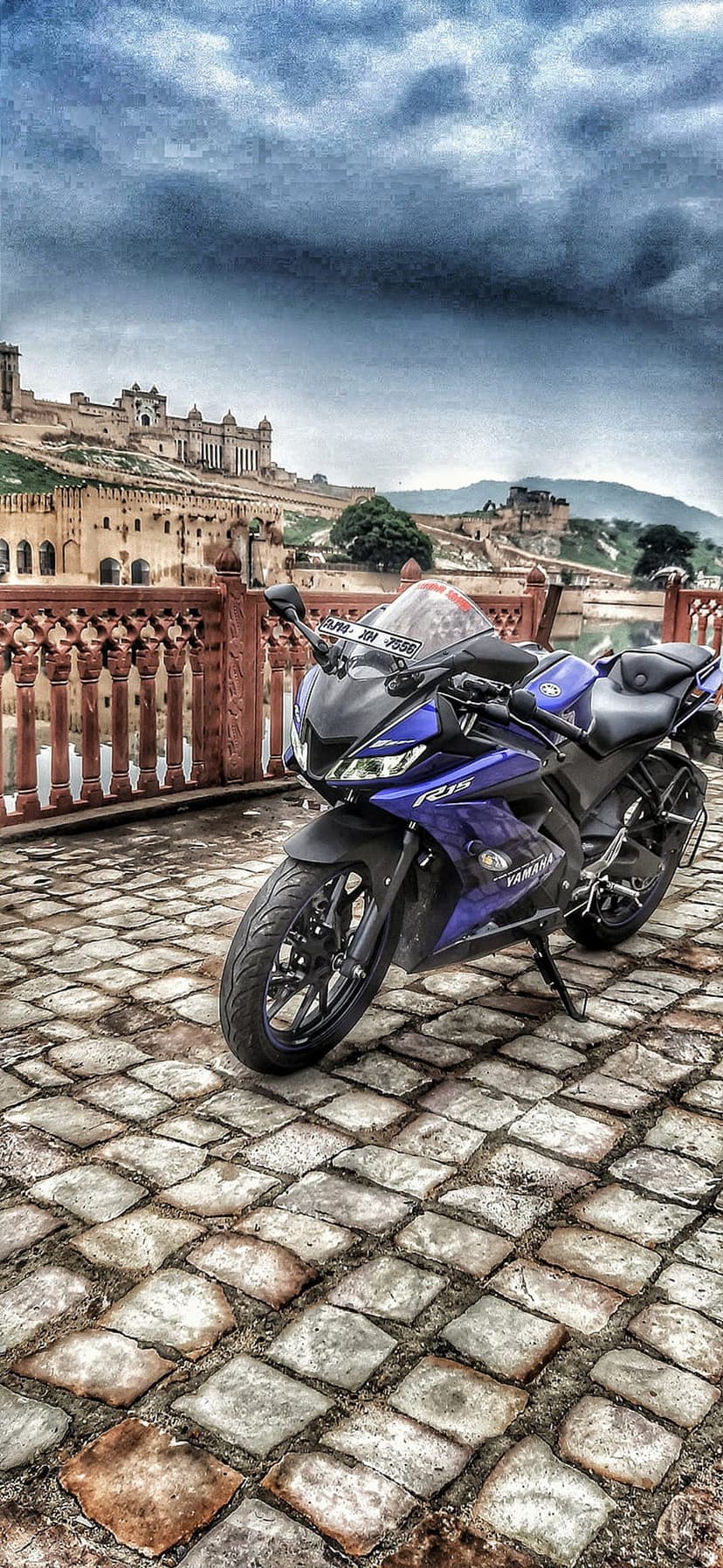 Blue Yamaha R15 motorcycle on a cobblestone path in front of the massive Amber Fort walls in Jaipur, India.