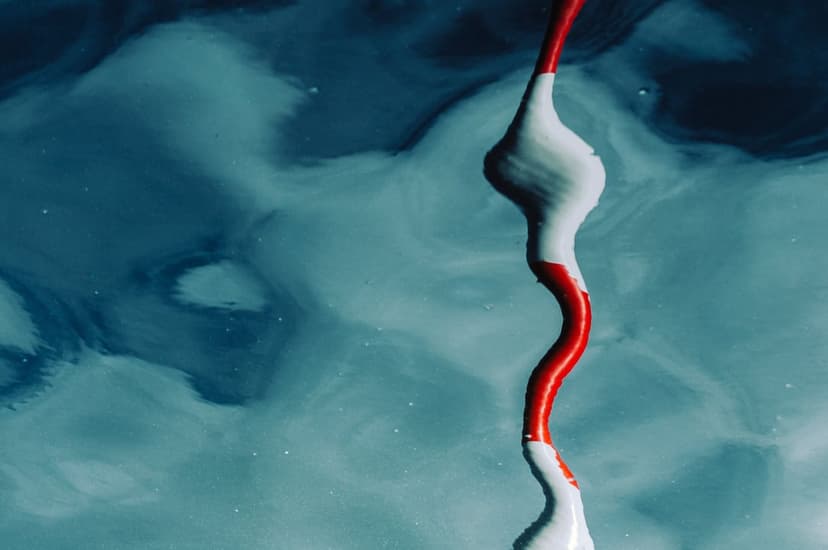 Crimson and white paint droplets suspended in a turbulent blue liquid with swirling textures and micro bubbles.