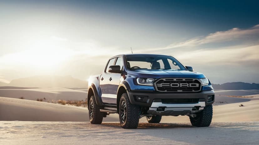 Blue Ford Ranger Raptor pickup truck on white sand dunes at sunset with warm golden lighting.
