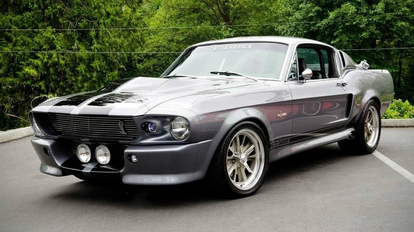 Silver Ford Mustang Shelby GT500 Eleanor with black stripes parked on asphalt with green trees background.