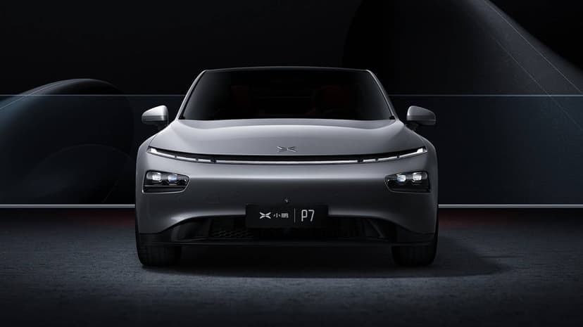 Front view of a silver Xpeng P7 electric sedan with glowing LED lights in a dark, minimalist studio setting.