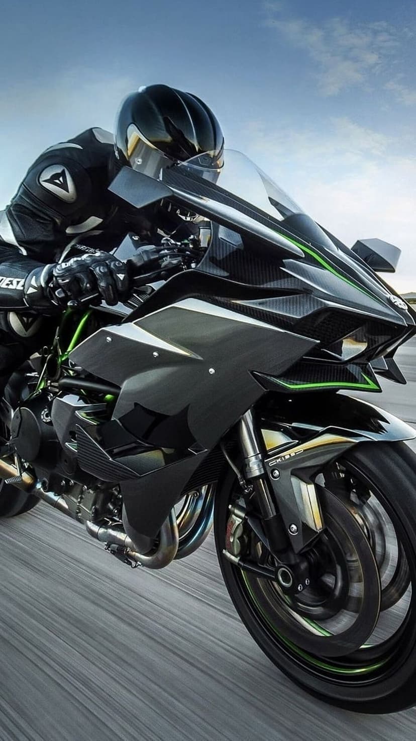 Kawasaki Ninja H2R motorcycle with a rider in a black suit speeds down a blurred road under a cloudy sky.