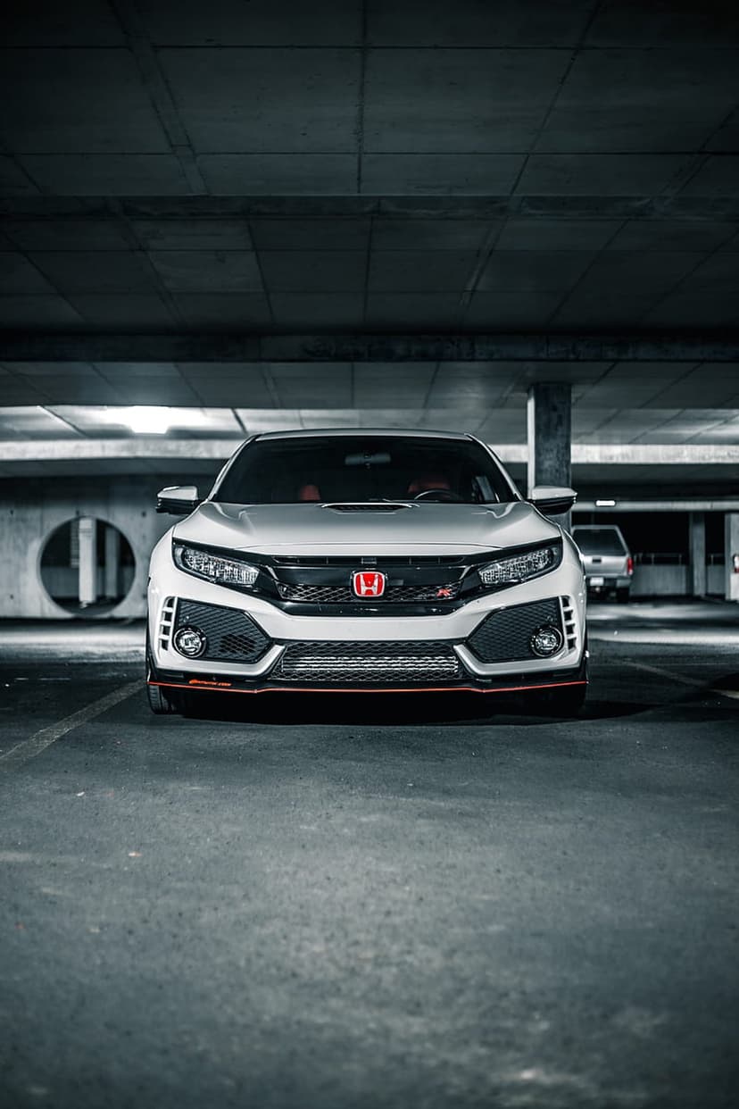 White Honda Civic Type R with red trim parked between concrete pillars in a dimly lit underground parking lot.