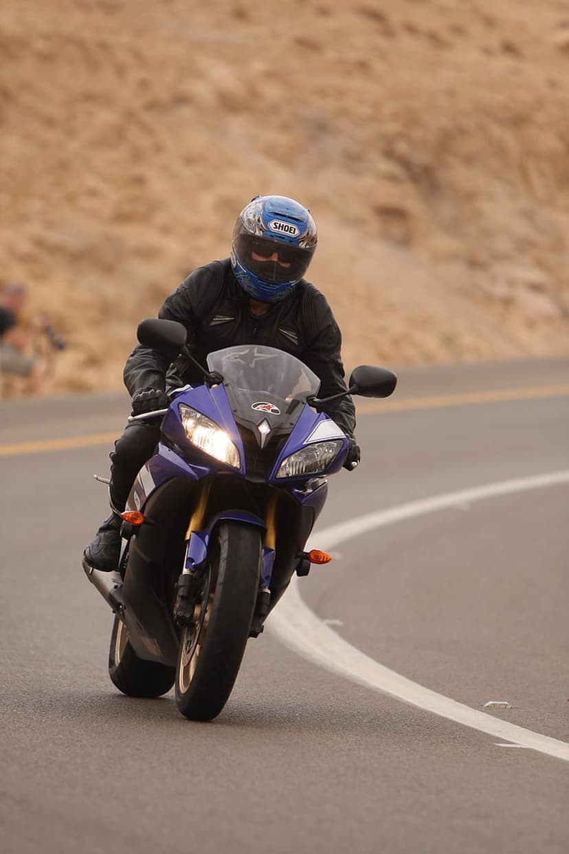 Motorcyclist in a blue helmet leans a purple sportbike into a sharp curve on a gray asphalt mountain road.