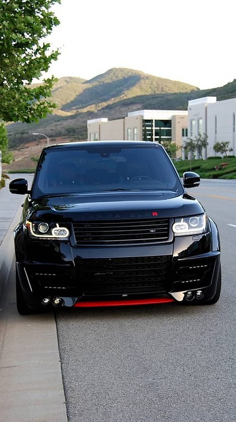 Black Range Rover with a custom body kit and red accents parked on a suburban street near modern buildings.