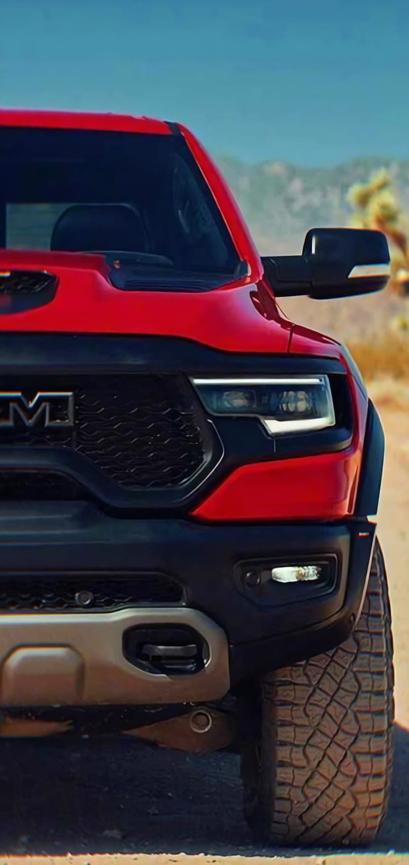 Red Ram TRX truck with an aggressive front grille and LED lights on a dusty desert road with mountains.