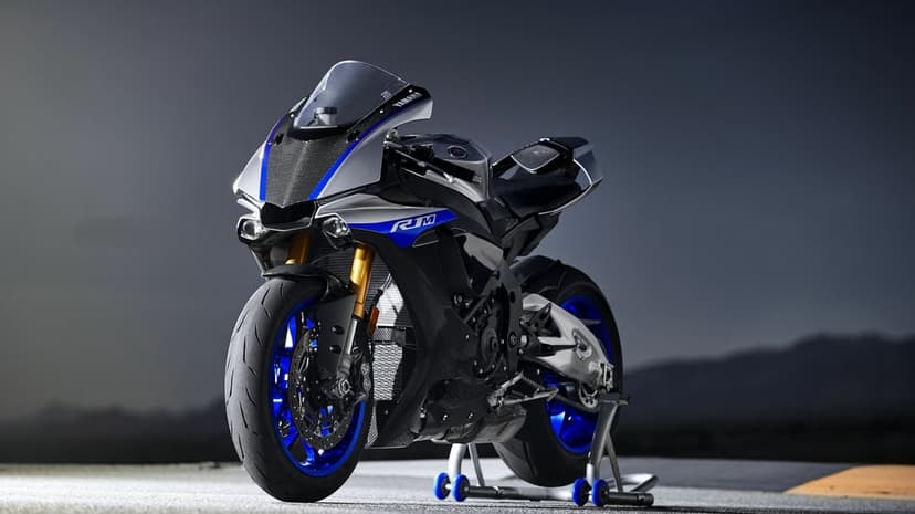 Silver Yamaha YZF-R1M motorcycle with blue wheels on a paddock stand under dramatic studio lighting.