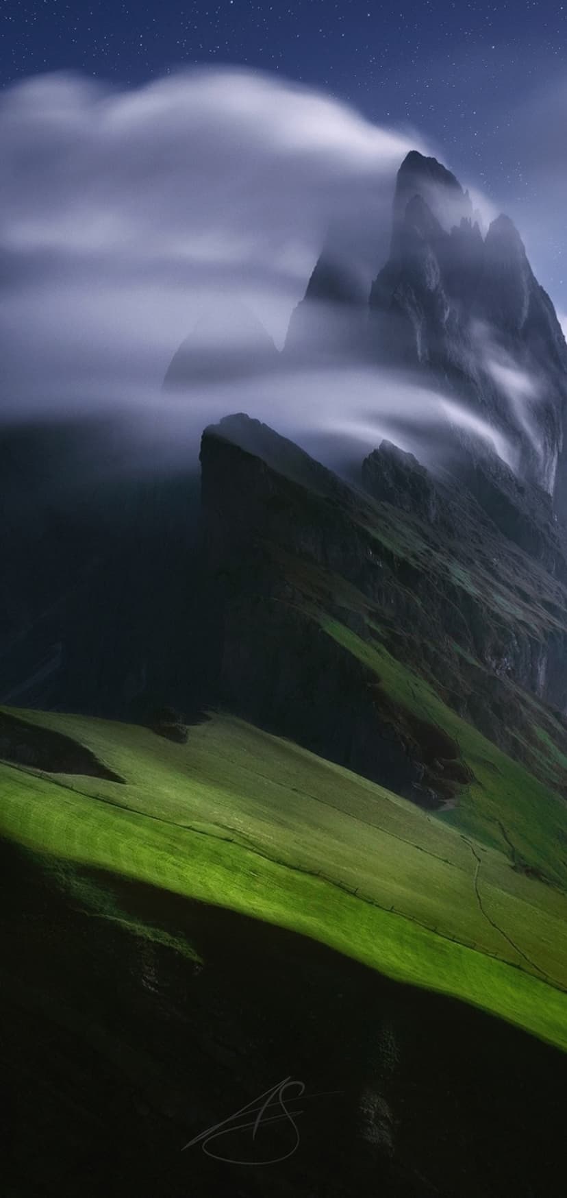 Jagged Seceda mountain peaks rise above swirling white mist and green alpine meadows under a deep blue sky.
