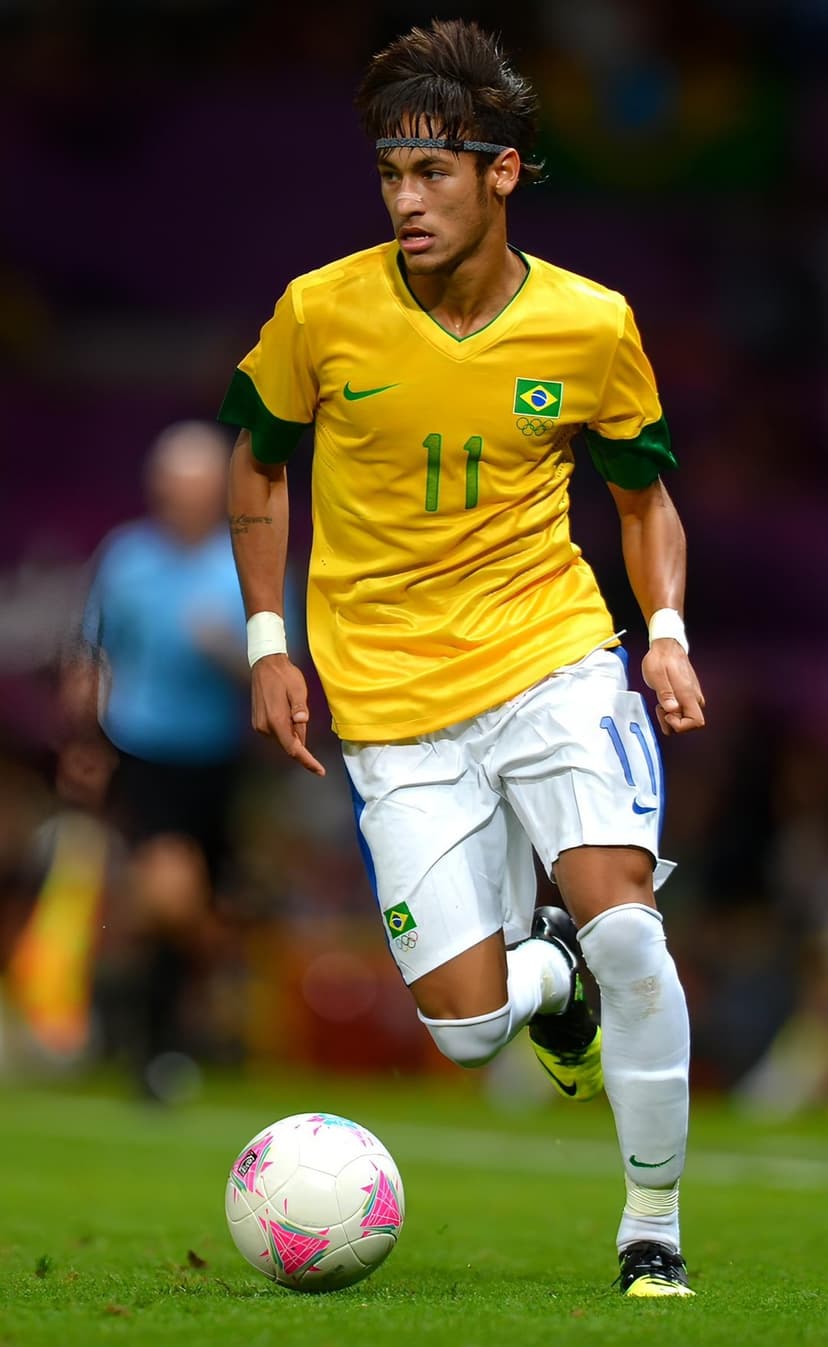 Neymar Jr in a yellow Brazil kit dribbles a soccer ball during an Olympic game on a green stadium pitch.