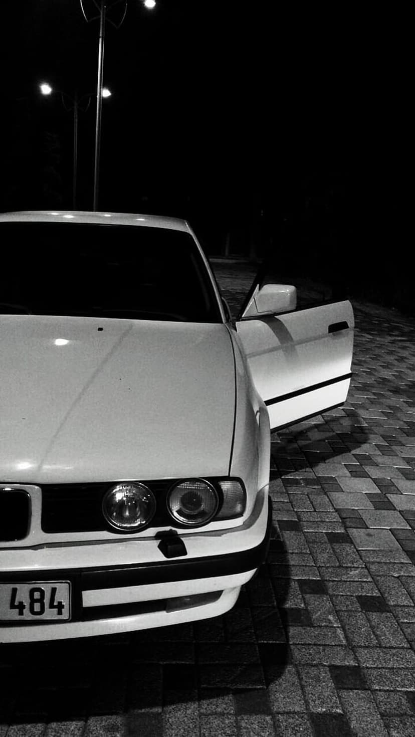 White vintage car with an open door parked on a dark street under bright lamps in high-contrast monochrome.