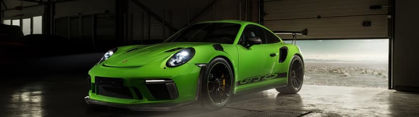 Green Porsche 911 GT3 RS with headlights on inside a dark garage with an open door looking out to a desert view.