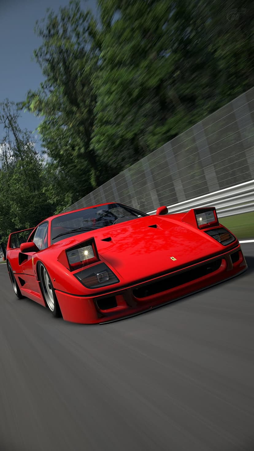 Red Ferrari F40 racing on a blurred track with green trees and a cloudy sky visible from a low-angle view.