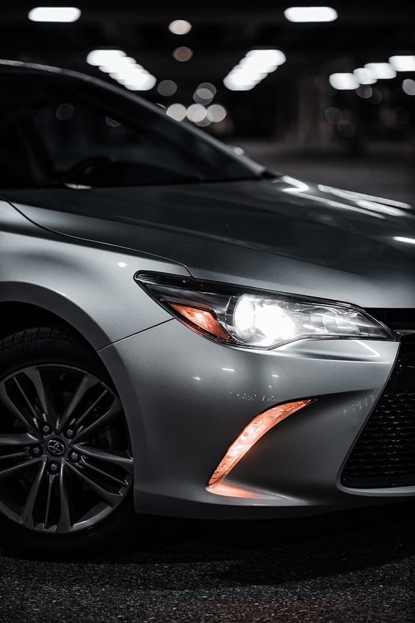 Toyota Camry LED headlight and alloy wheel in a dark parking garage with amber accent lights and bokeh background.