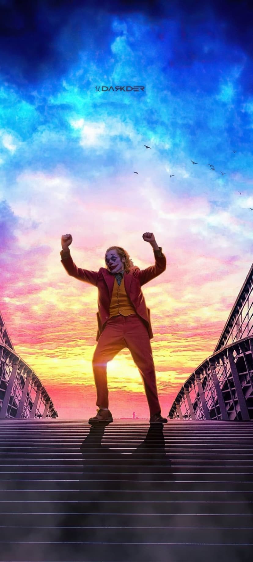Joker dances on stone stairs with arms outstretched against a purple and orange sunset sky framed by a bridge.