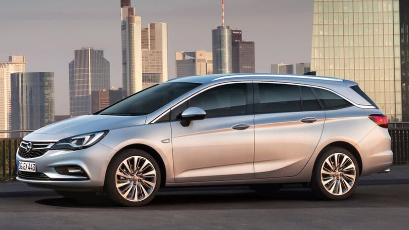 Silver Opel Astra Sports Tourer parked in front of a modern city skyline with skyscrapers under a soft sky.