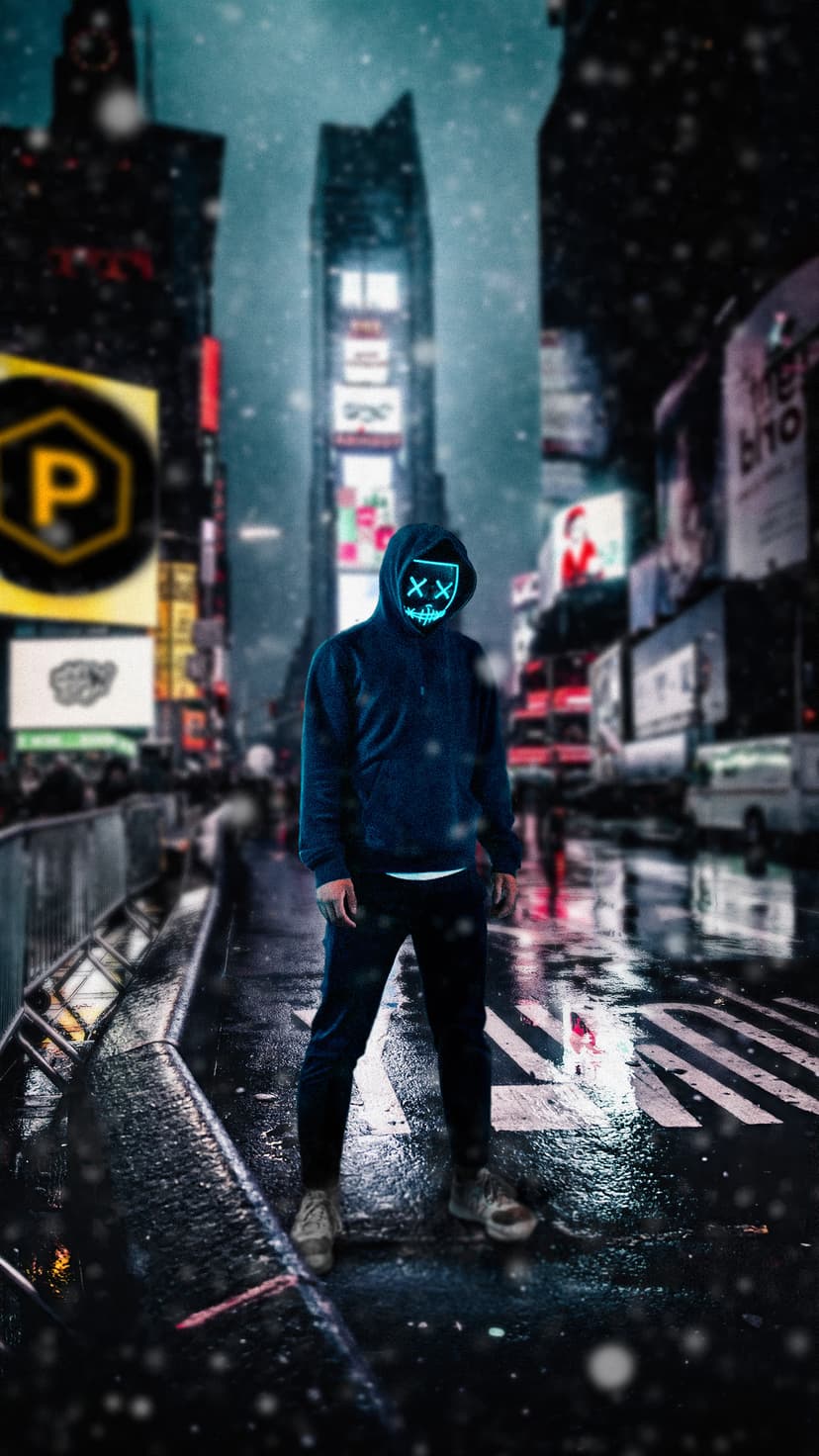 Hooded person wearing a glowing blue X mask on a wet city street at night with blurred neon lights in the distance.