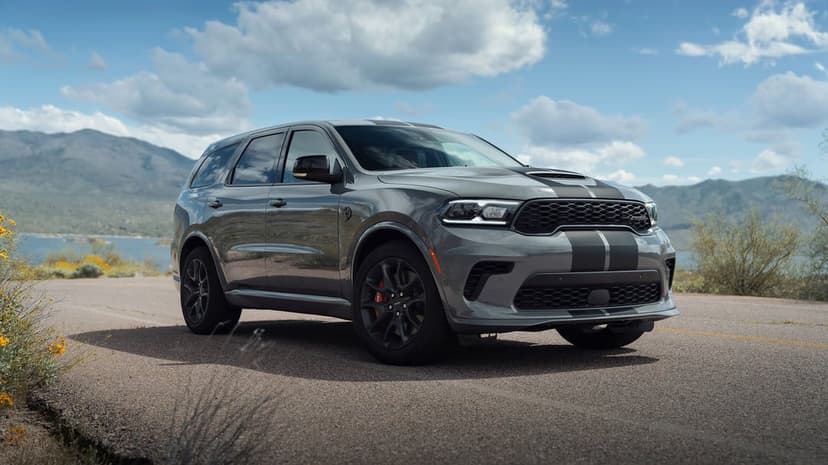 Gray Dodge Durango SRT SUV with black racing stripes parked on an asphalt road against a scenic mountain backdrop.