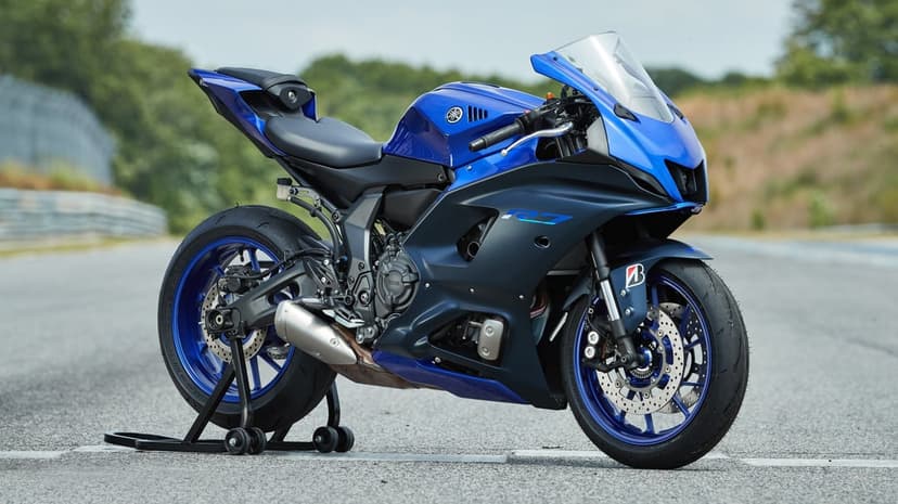 Blue and matte black Yamaha YZF-R7 motorcycle on a rear stand at a racing track with blurred greenery background.