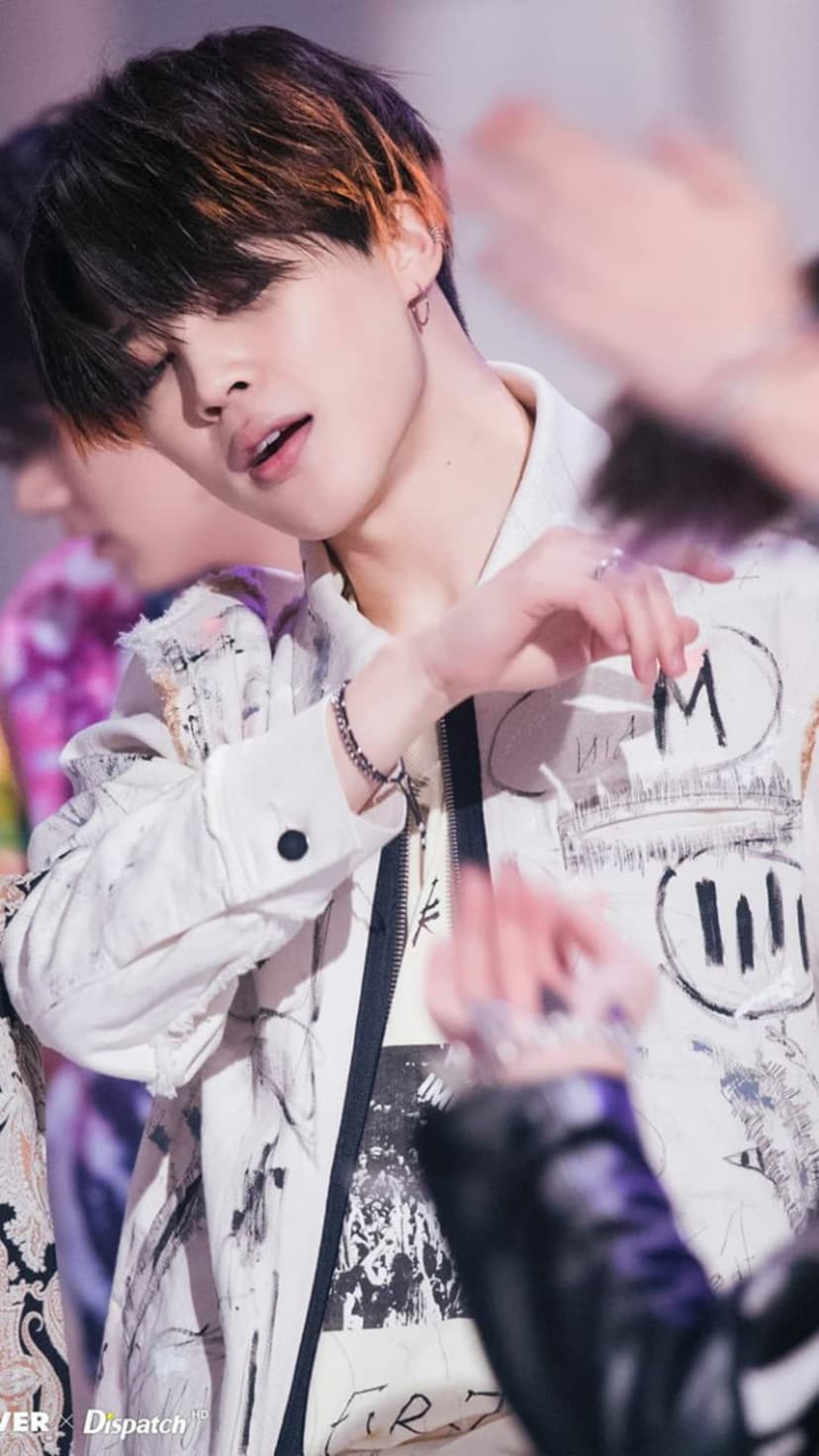 Park Jimin of BTS tilts his head down wearing a white graffiti-print jacket and silver rings during a concert.