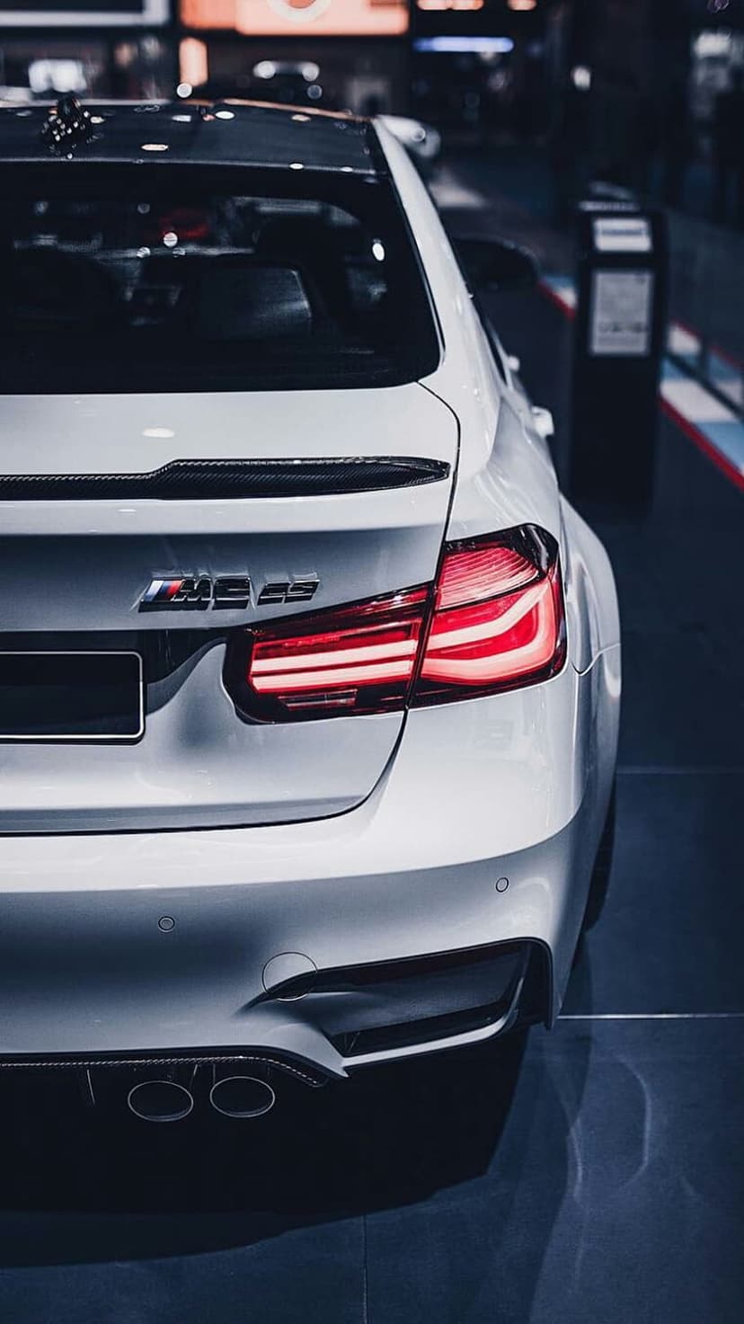 White BMW M4 CS rear taillights, carbon fiber spoiler, and quad exhaust pipes on a high-performance sports car.