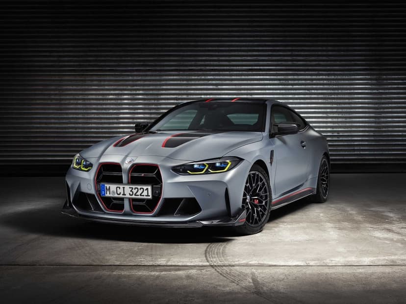 Matte grey BMW M4 CSL with red grille accents and yellow headlights in a dark industrial garage.