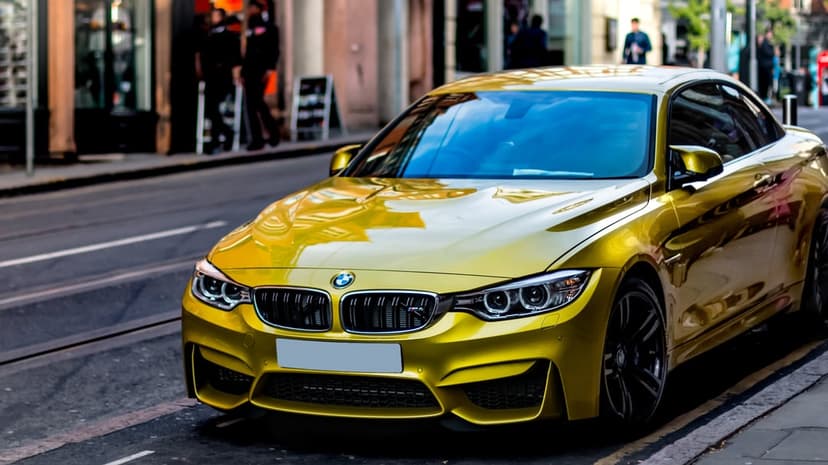 Front view of a metallic yellow BMW M4 coupe parked on a city street with a blurred urban background.