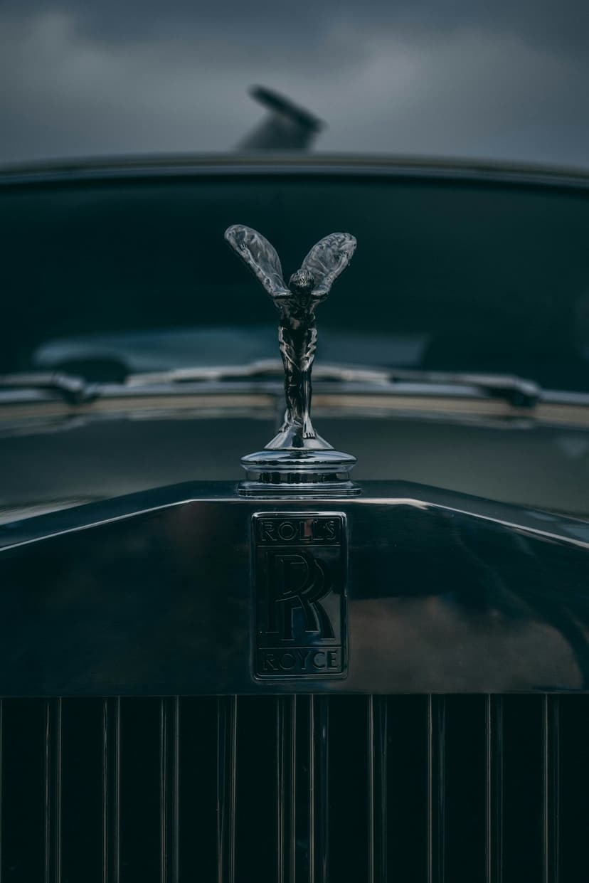 Spirit of Ecstasy mascot sits on a chrome radiator grille reflecting a gray sky with sharp metallic highlights.