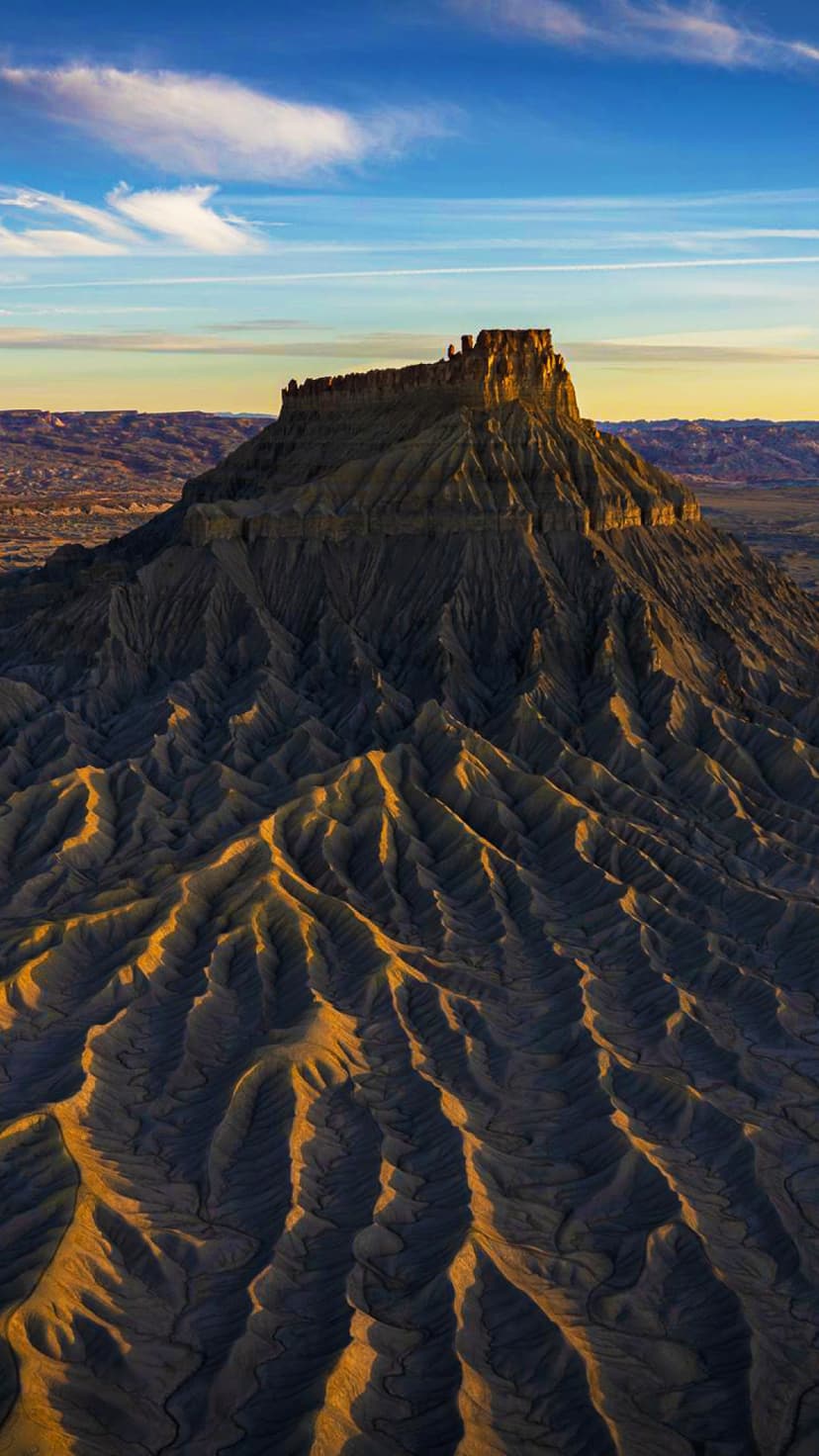 Factory Butte mountain with eroded grey slopes and a sunlit peak stands under a soft blue and orange dusk sky.