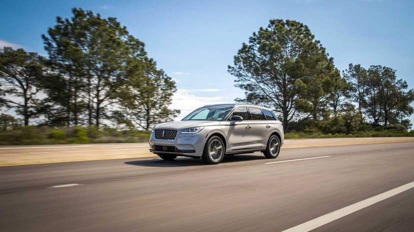 Silver Lincoln Corsair SUV driving on a sunlit highway with green trees and a blue sky in the background.