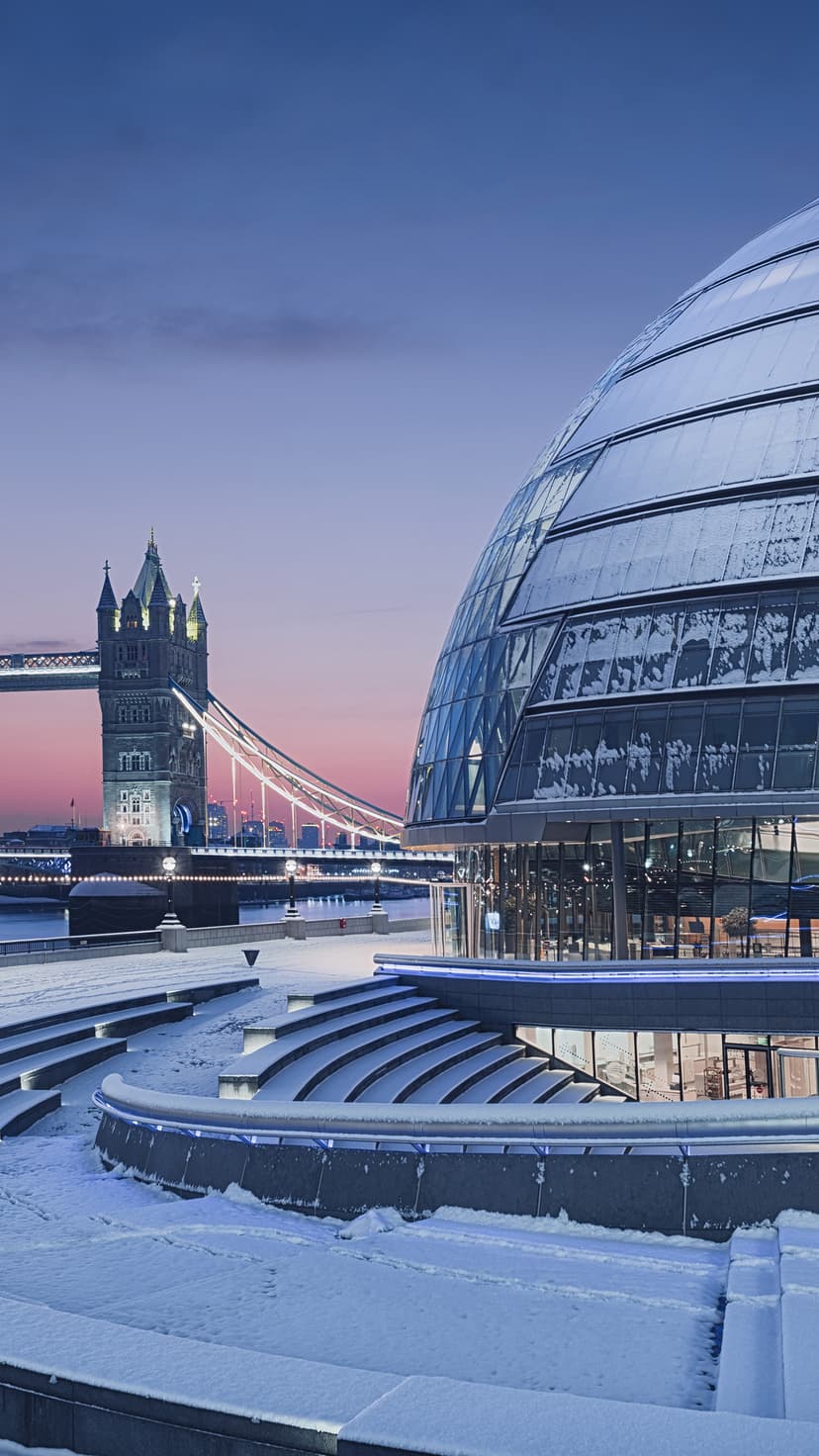 Tower Bridge and City Hall covered in snow during a pink twilight evening in London overlooking the Thames.