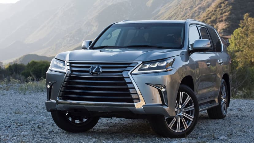 Silver Lexus LX 570 SUV parked on a gravel trail with misty mountains and soft sunlight in the background.