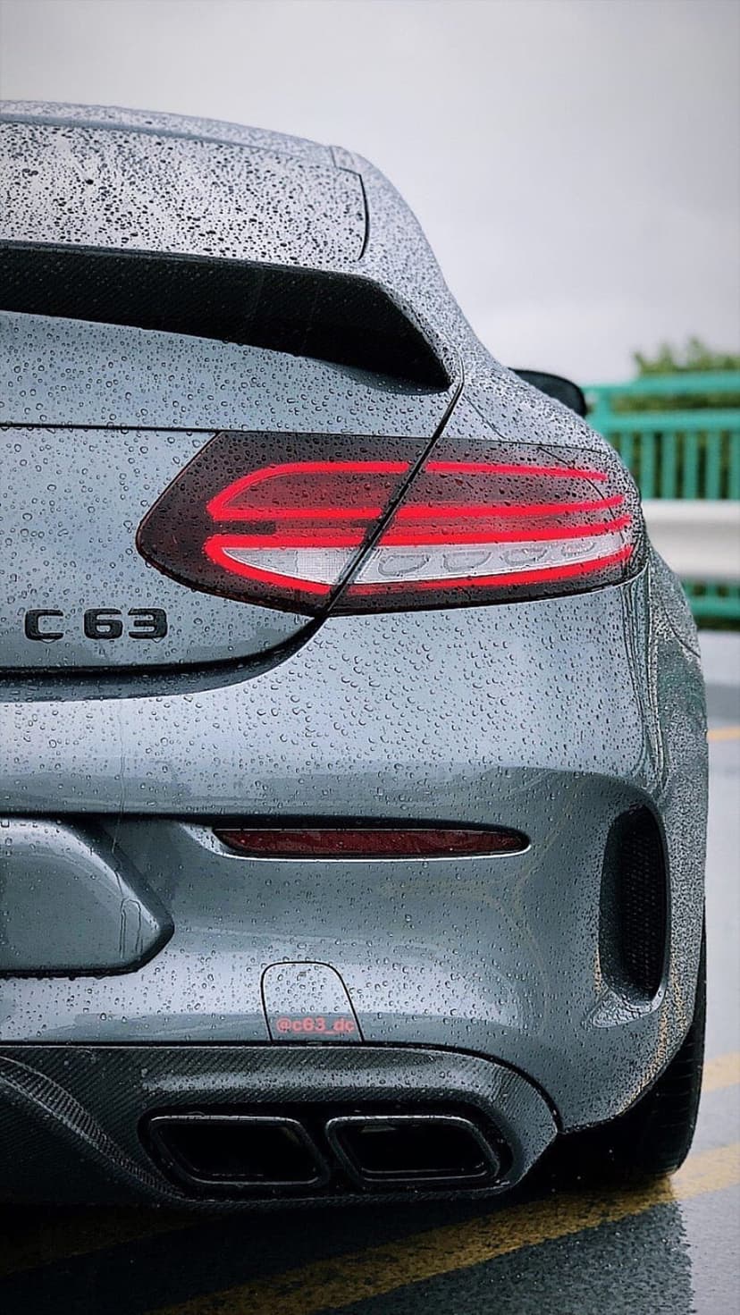 Mercedes-AMG C63 rear LED lights and quad exhausts covered in raindrops on a wet grey car body in the rain.