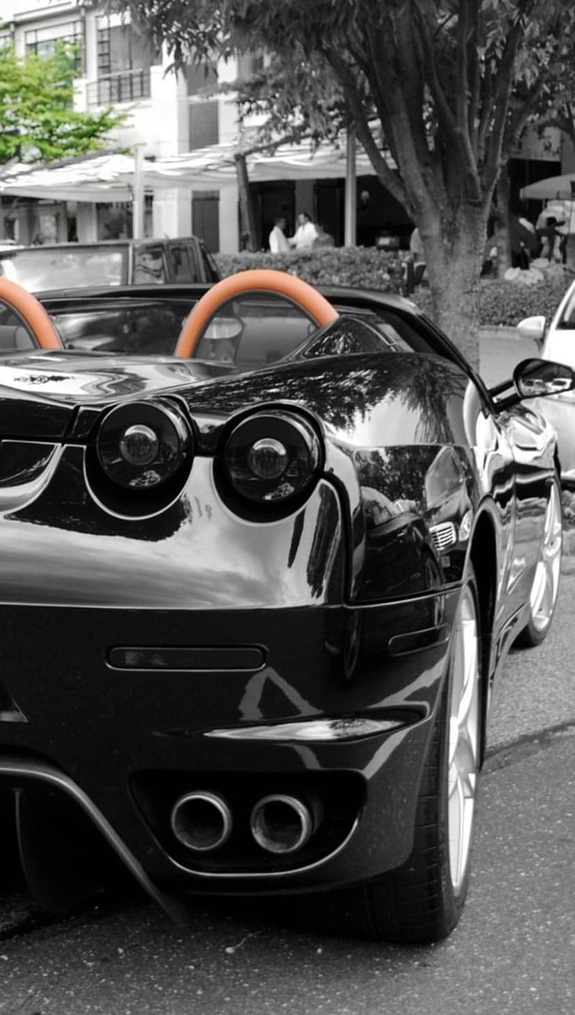 Black roadster rear view showing circular red taillights, silver exhausts, and a bright orange interior accent.