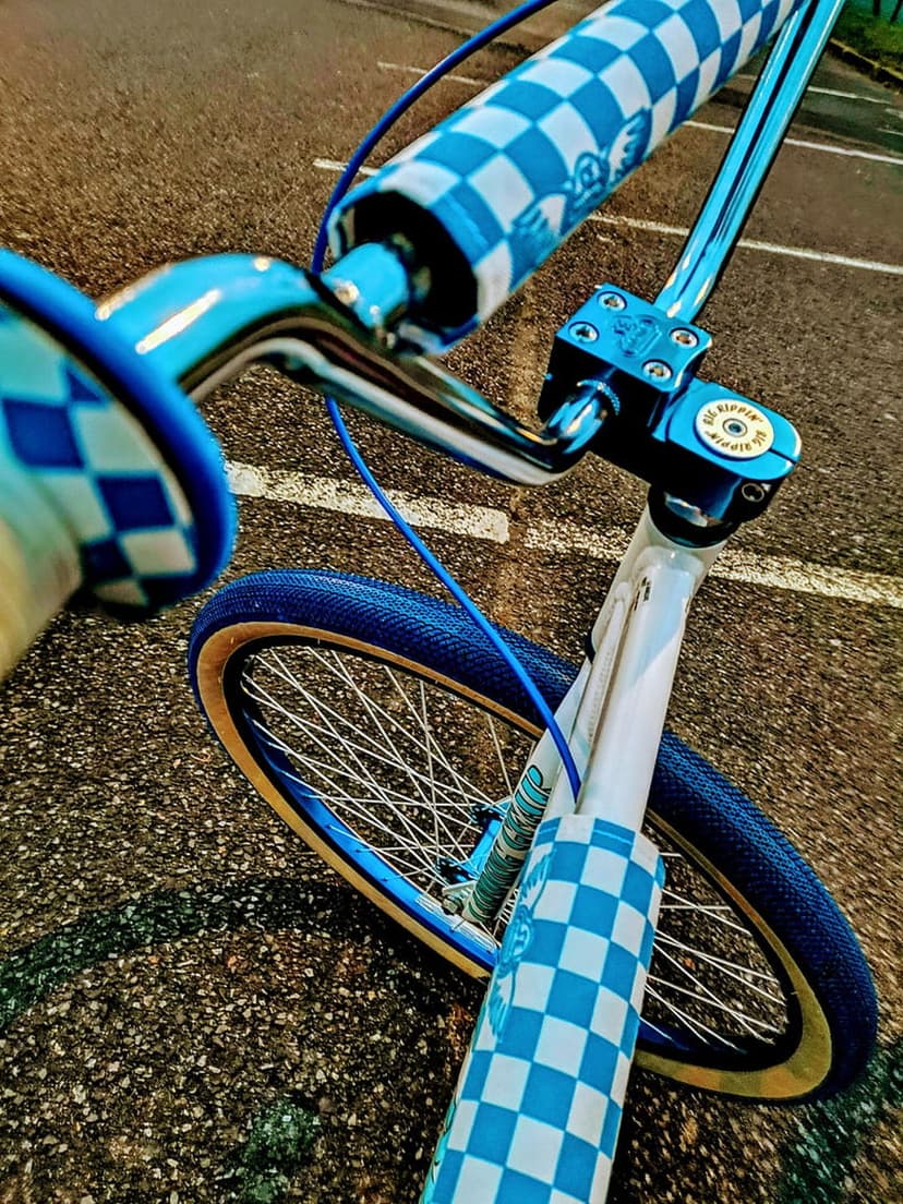 Blue and white checkerboard BMX bike grips on chrome handlebars with a vibrant blue tire in a close-up shot.