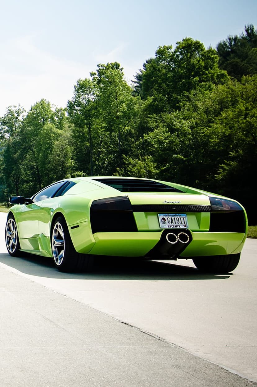 Lime green Lamborghini Aventador rear view with double exhausts parked on asphalt before a lush green forest.