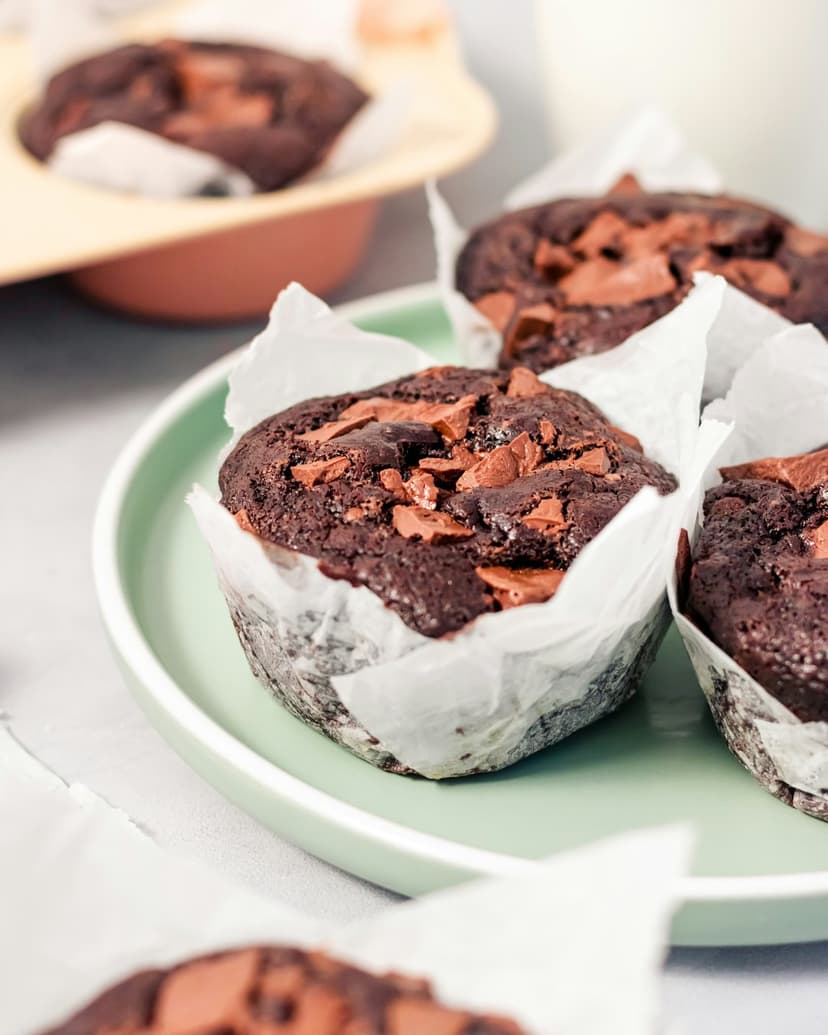 Chocolate muffins with dark chunks sit on a light green plate, showing soft textures and crumbs in close-up.