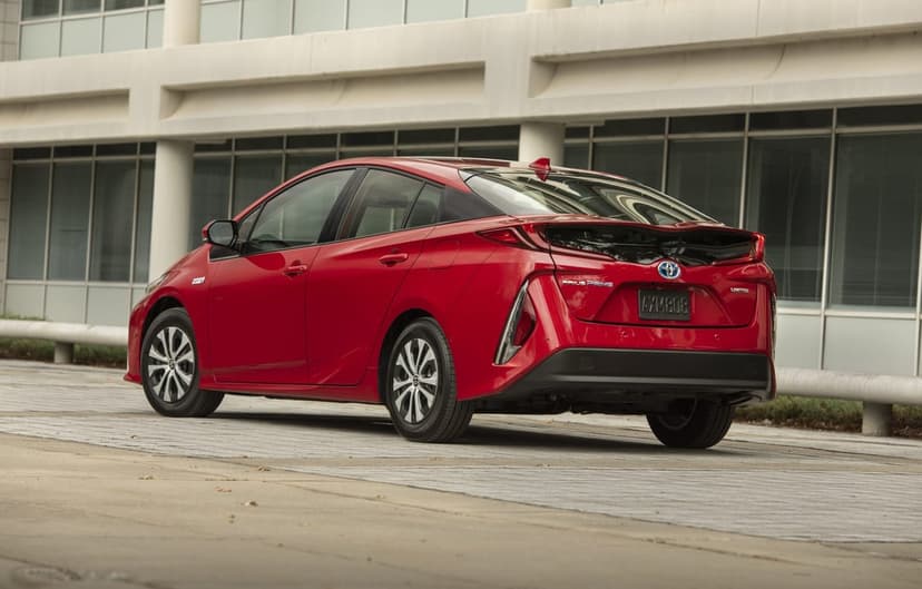 Red Toyota Prius Prime parked in front of a modern white building with large windows and concrete pillars.