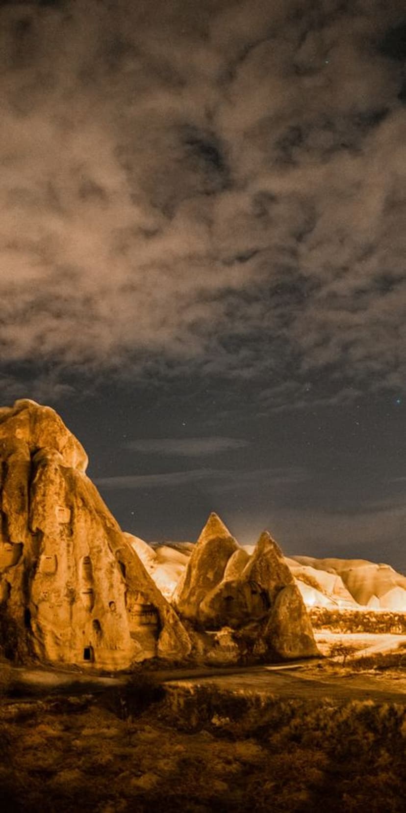 Tall conical rock formations rise into a cloudy night sky illuminated by soft moonlight in a deep valley.