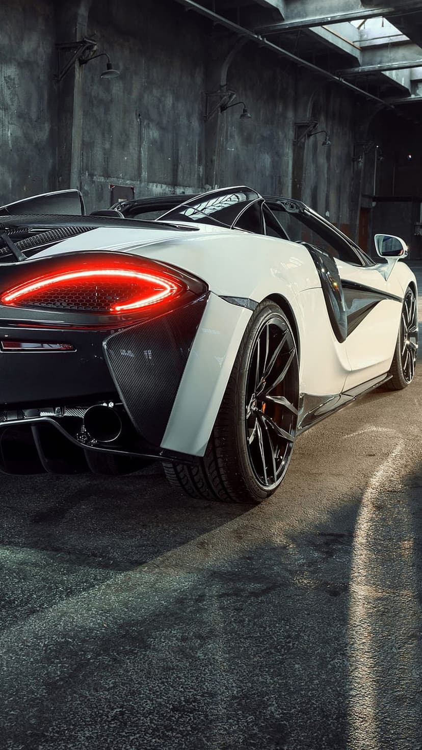 White McLaren convertible supercar with glowing red taillights parked on a concrete floor in a dark garage.