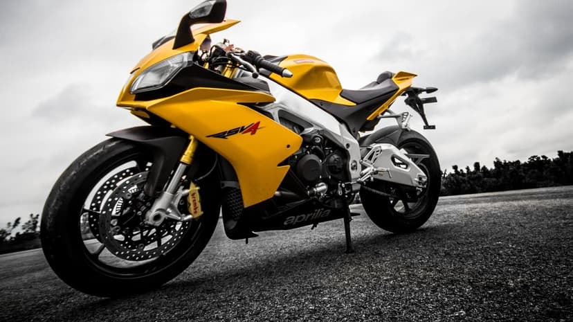 Vibrant yellow Aprilia RSV4 motorcycle parked on a grey asphalt track under a moody, desaturated overcast sky.