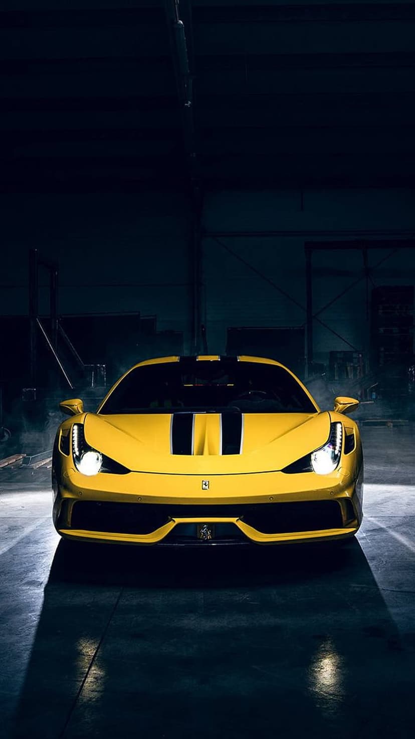 Yellow Ferrari 458 Italia with black racing stripes and glowing headlights parked on a reflective indoor floor.