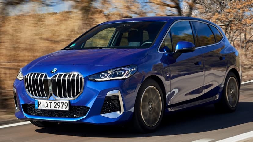 Blue BMW 2 Series Active Tourer driving fast on a sunlit road with a blurred autumn-toned landscape background.