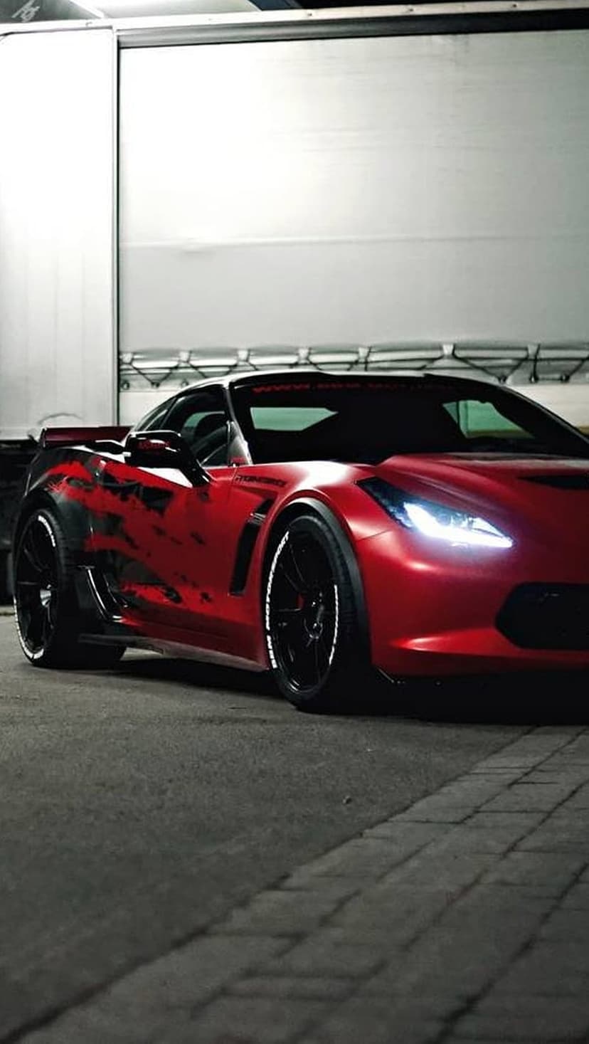 Red Corvette Z06 with custom graphics and white tire lettering parked before an industrial metal door.