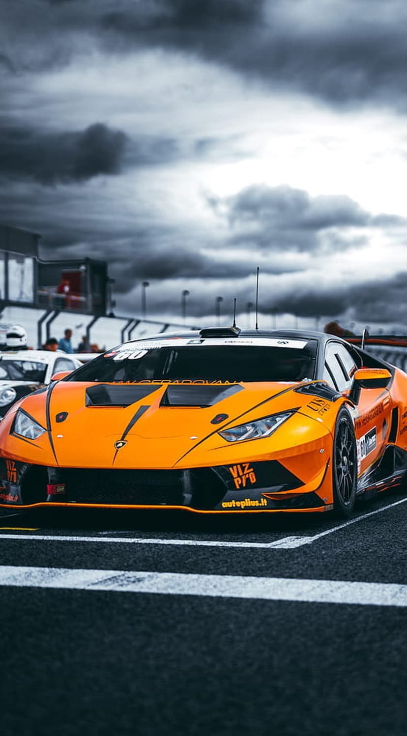 Orange Lamborghini Huracan race car with aerodynamic wings parked on a circuit under a dark and stormy sky.