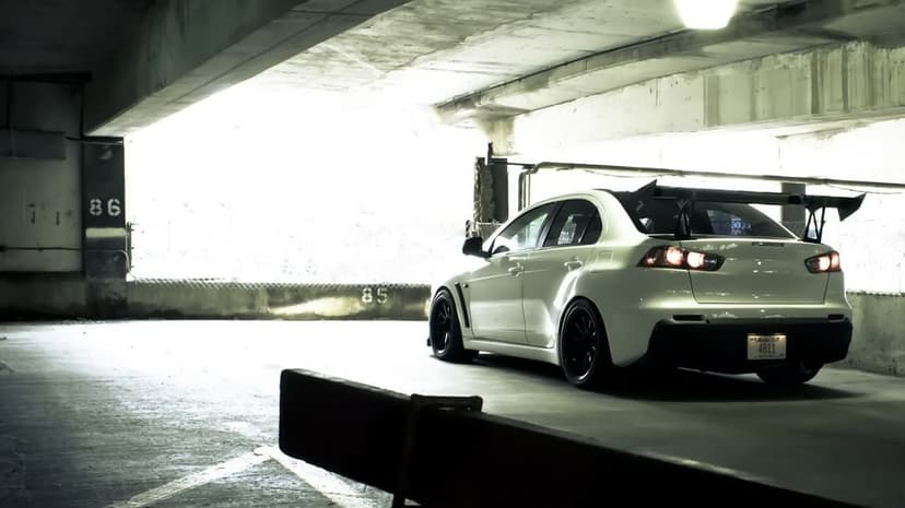 Rear view of a white Mitsubishi Lancer Evo X with a large wing in a dimly lit concrete parking garage.
