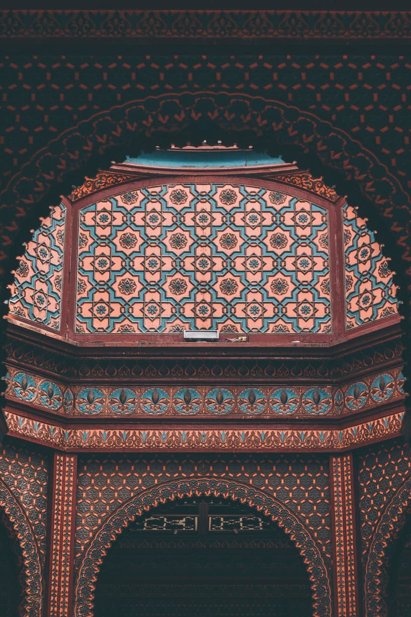 Teal and coral geometric zellij tiles are framed by dark wooden arches in a detailed architectural close-up.