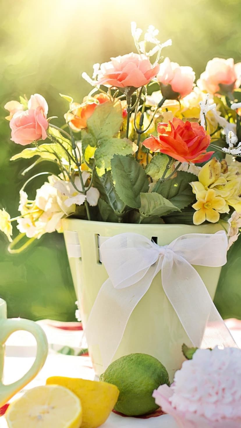 Citrus fruits and a pink cupcake sit beside a floral bouquet on a sunlit table in a lush garden setting.