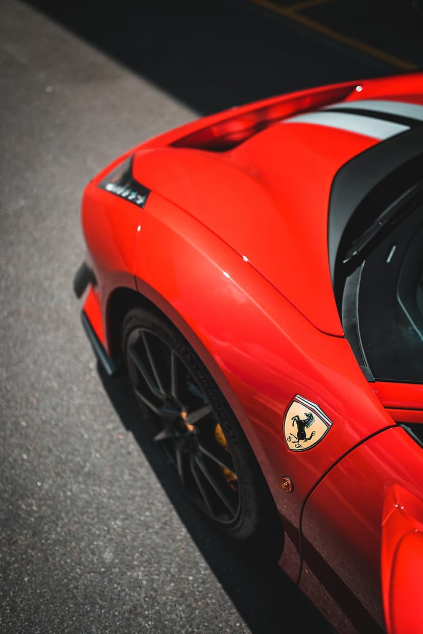 Red Ferrari fender with a Prancing Horse shield, black alloy wheel, and yellow brake calipers on asphalt.